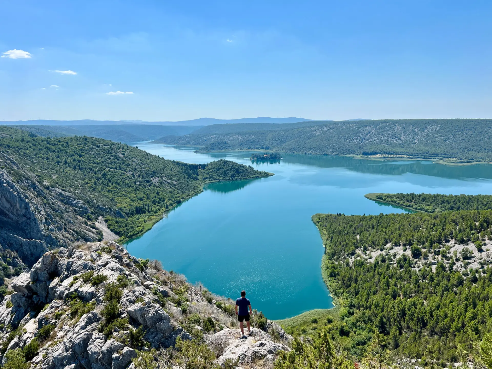 A member of the Olam team standing on a rocky ridge above a turquoise river winding through green hills