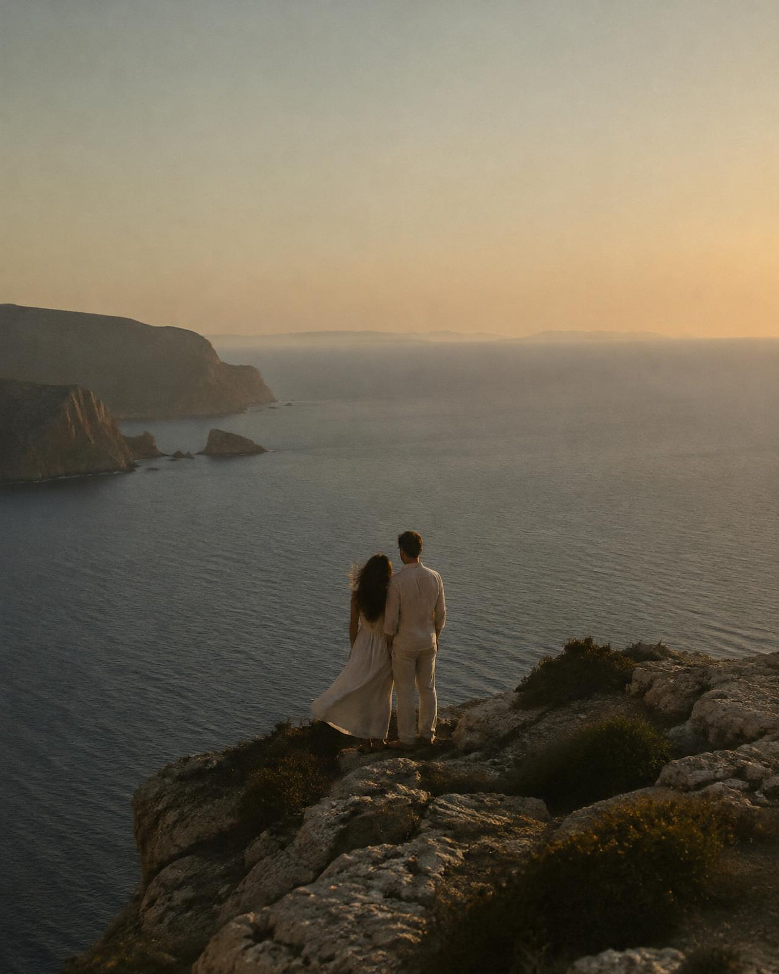 A couple on a cliff above a calm sea at sunset